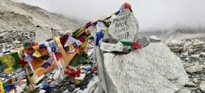 Everest Base Camp Trek via Salleri-Large stone marker painted with "Everest Base Camp 5364M" and draped in colorful Buddhist prayer flags on the Khumbu Glacier in Nepal.
