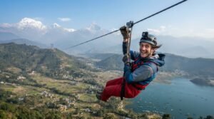 A traveler with a joyful expression riding the high-speed ZipFlyer in Pokhara, Nepal, suspended over the valley, Phewa Lake, and the Annapurna mountain range.