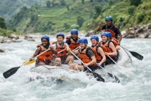 Seti River Rafting in Pokhara-Group of rafters in orange life jackets and blue helmets laughing and paddling in whitewater with a green hill background.