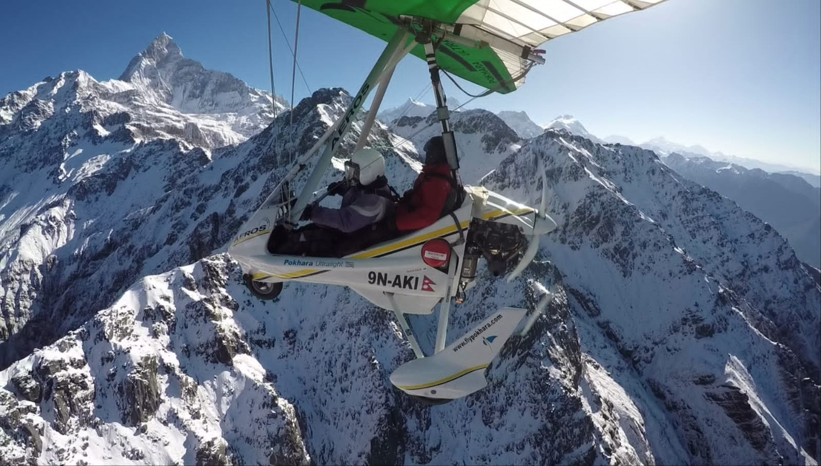Ultralight Flight in Pokhara-A white motorized light aircraft flying close to massive snow-covered Himalayan mountains, with a pilot looking out the window.