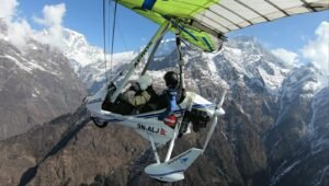 Ultralight Flight in Pokhara-yellow and white ultralight trike aircraft carrying two passengers flying over a steep, snow-covered mountain ridge.