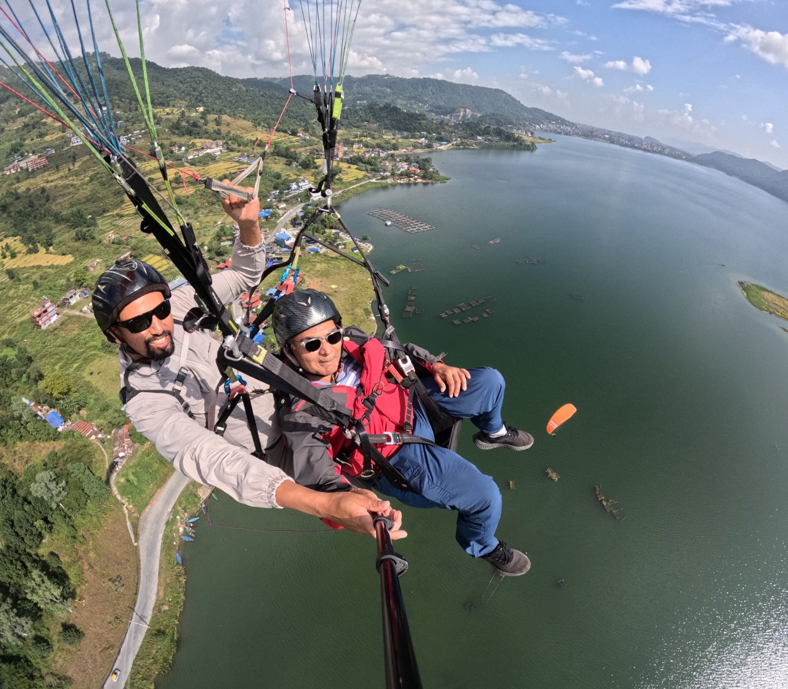 Paragliding in Pokhara-Close-up of a red paragliding wing overhead, with two men in helmets and safety gear looking out over a landscape.