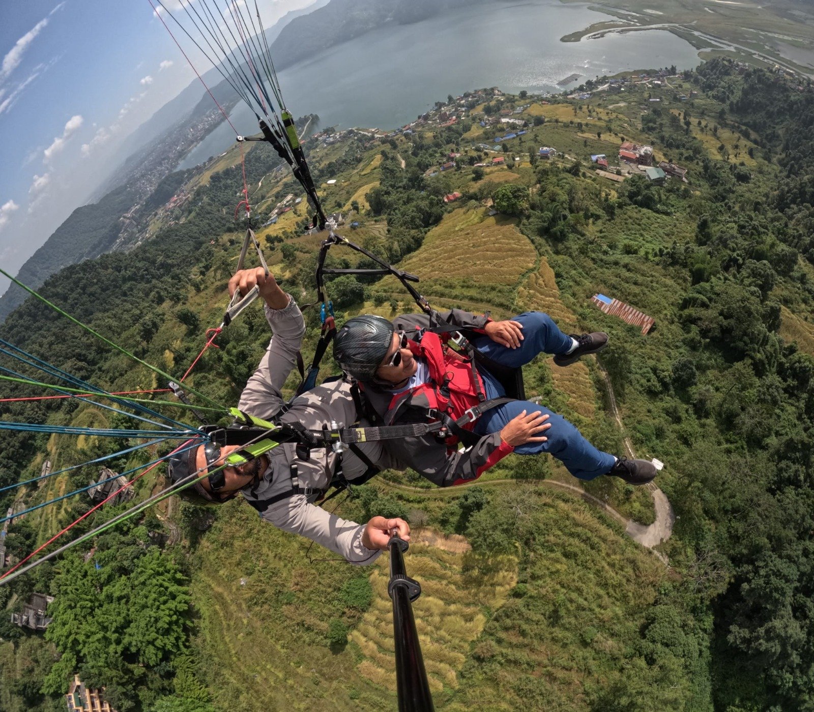 Paragliding in Pokhara-Tandem paragliders flying high with a dramatic backdrop of expansive mountain ranges and a large lake stretching into the distance.
